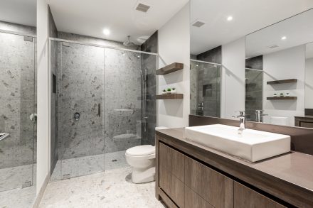 Aménagement intérieur d'une salle de bain moderne et épurée armoires foncées et douche en verre.